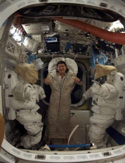 Figure 11.7. Tucked away in a sleeping bag, an astronaut poses near two extravehicular spacesuits in the airlock of the ISS (Courtesy of NASA).